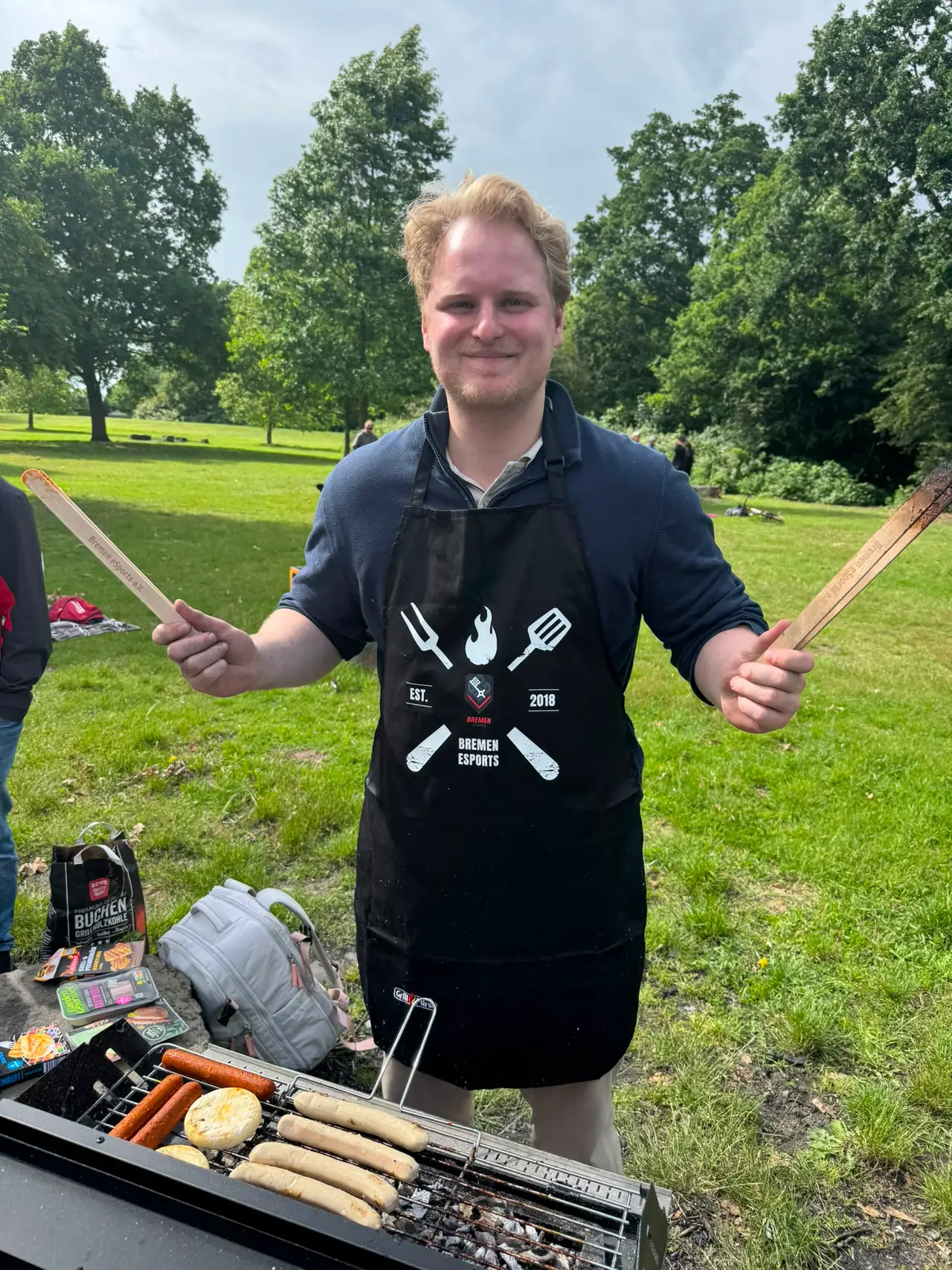 Grillmeister Louis steht im Park am Grill und präsentiert den HBeS Grillmerch