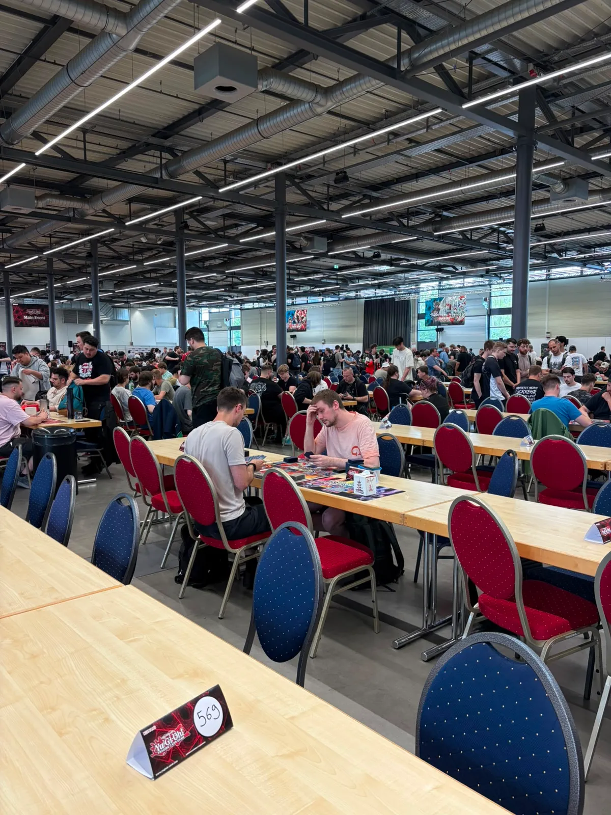 Blick auf die Turnierfläche mit vielen Tischen und Teilnehmenden in der Halle